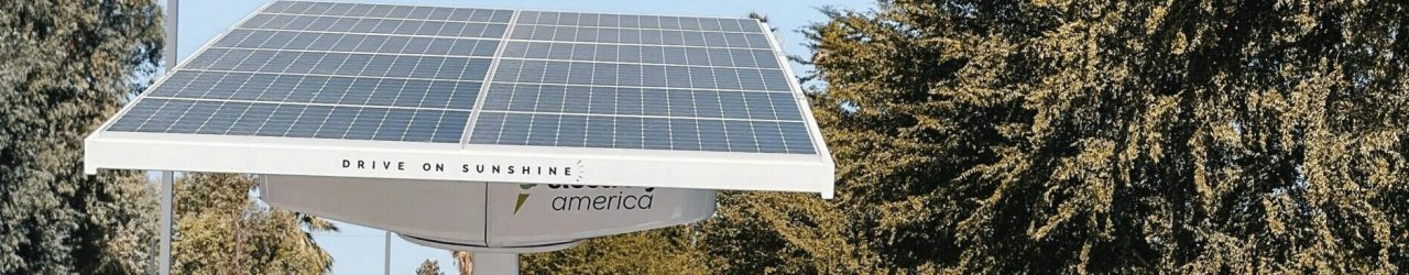 A white electric car charging under a solar panel in an urban setting, showcasing renewable energy use.